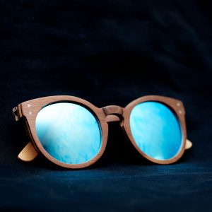 Skateboard. Puukehyksiset käsintehdyt aurinkolasit sinisillä peililinsseillä. Suunniteltu Suomessa planeettaa kunnioittaen. Kestävästi valmistettu afrikkalaisista kierrätysmateriaaleista. Handcrafted wooden framed sunglasses with blue mirror lenses. Designed in Finland with respect for the planet. Sustainably made from recycled African materials.